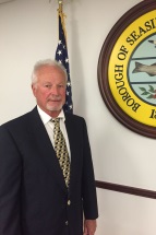 Council Member Kraft standing in front of the American Flag and the Borough Seal